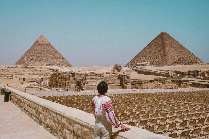 Ilustração corporativa das pirâmides do Egito ao entardecer com camelos e turistas na base